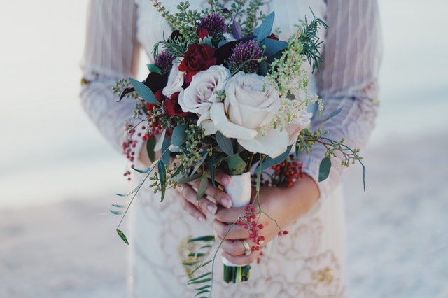 Žena v svadobných šatách drží pred sebou farebnú kyticu z kvetov.jpg